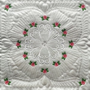May include: White quilted fabric with a delicate floral design. The design features a central circle with a swirling pattern and small pink roses with green leaves around the edges.