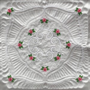 May include: White quilted fabric with a repeating pattern of pink roses and green leaves. The quilting design features a central circle with swirls and a square frame with a scalloped edge.