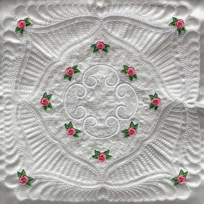 May include: White quilted fabric with a repeating pattern of pink roses and green leaves. The quilting design features a central circle with swirls and a square frame with a scalloped edge.