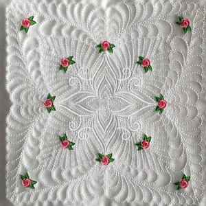May include: White quilted fabric with a floral design. The fabric is quilted in a pattern of small circles and has a central design of a large flower with smaller flowers around it. The flowers are pink with green leaves.