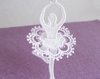 May include: White lace ballerina ornament with a delicate floral design. The ornament is hanging from a gold string.