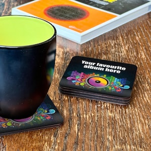 May include: A set of four black square coasters featuring a colourful music-themed design. The design includes a large speaker with rainbow-coloured sound waves and musical notes. The text "Your favourite album here" is printed on the coaster.