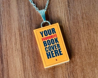 May include: A silver-toned metal chain necklace featuring a rectangular pendant shaped like a miniature book. The pendant has an orange cover with black text that reads YOUR FAVOURITE BOOK COVER HERE, with the word FAVOURITE printed in red.