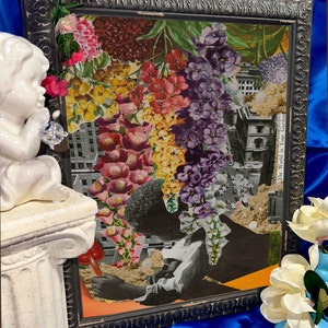 Pu&ograve; includere: Un'opera d'arte in collage incorniciata che presenta un arrangiamento floreale colorato con una citt&agrave; sullo sfondo. L'opera d'arte &egrave; intitolata "The World in Your Garden".