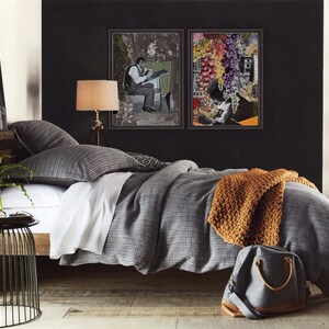 Pu&ograve; includere: Un letto con motivo grigio e bianco con una coperta di maglia marrone e una borsa da viaggio grigia. Il letto &egrave; contro un muro nero con due stampe d'arte in bianco e nero incorniciate.