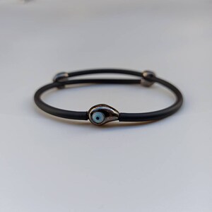 Unisex, adjustable, black rubber, evil eye bracelet, with a black rhodium plating.