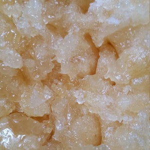 May include: Close-up of a light brown, translucent, honey-like substance with a grainy texture.