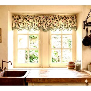 May include: A window valance featuring a floral pattern with red, blue, and green botanical elements on a cream background. The fabric has a scalloped bottom edge with a light green trim, gathered at the top to create a soft, pleated effect.