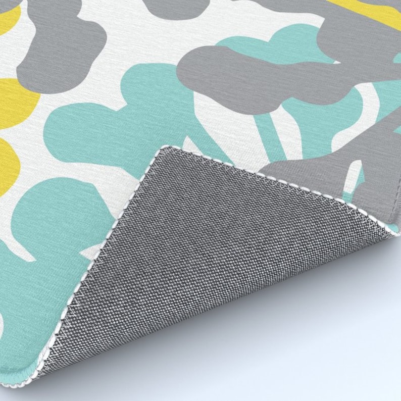 May include: A rug with a repeating pattern of abstract shapes in yellow, gray, and teal on a white background. The rug's edge is visible, showing a gray backing.