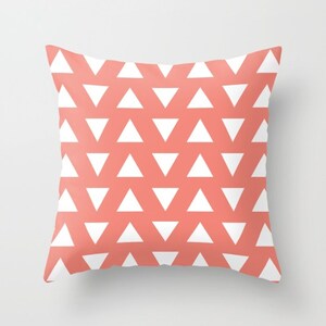 May include: Square coral cushion featuring a repeating pattern of white triangles. The triangles are evenly spaced across the cushion's surface, creating a geometric design. The cushion is a decorative item for a home.
