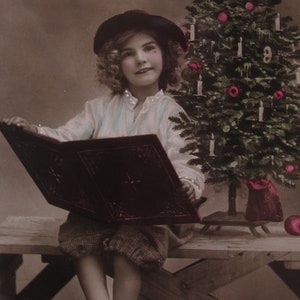 Glossy vintage postcard of a sweet little child reading a book next to the Christmas tree, old postcard, antique postcard Christmas
