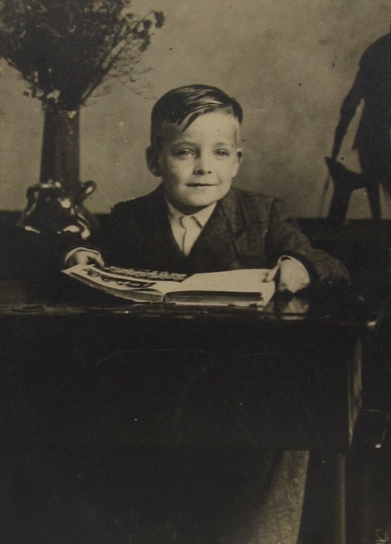 old photo postcard Vintage photo postcard of a cute boy sitting at an antique desk with a book