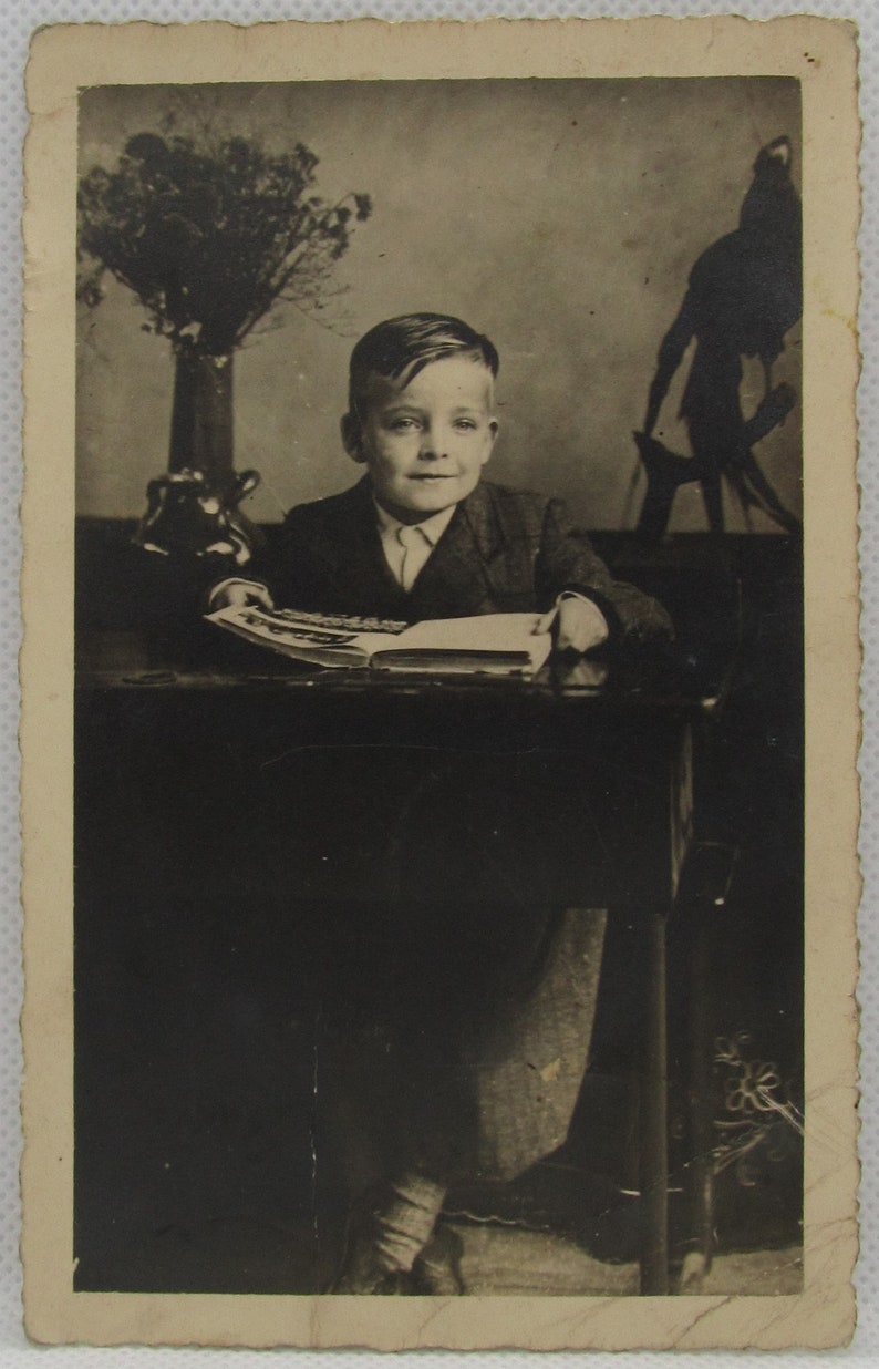 old photo postcard Vintage photo postcard of a cute boy sitting at an antique desk with a book