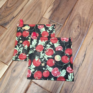 May include: Two black pot holders with a red tomato and green vine pattern. The pot holders have red hanging loops.