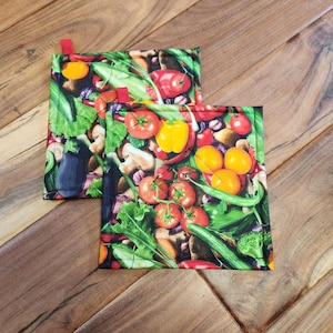 May include: Two colorful pot holders with a pattern of various vegetables, including tomatoes, peppers, onions, and green beans. The pot holders are made of fabric and have a quilted design.