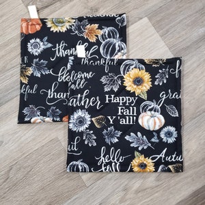 May include: Two black and white pot holders with a fall theme. The pot holders feature sunflowers, pumpkins, leaves, and the text "Thankful", "Welcome Fall", "Gather", "Happy Fall Y'all!" and "Hello Fall".