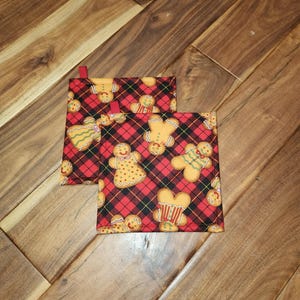 May include: Two red and black plaid pot holders with a gingerbread man design. The pot holders have red ribbon loops for hanging.