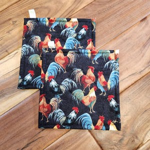 May include: Two black quilted pot holders with a rooster pattern. The roosters are colorful with red, yellow, blue, and green accents.