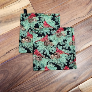 May include: Two black and green pot holders with a red cardinal and pine cone pattern.