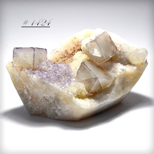 May include: A natural mineral specimen featuring cubic fluorite crystals in shades of purple and clear, set in a matrix of beige and cream-colored rock. The text "# 1424" is visible in the upper left corner.