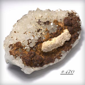 May include: A natural quartz crystal cluster with a mix of clear and brown hues. The crystal formation has a rough, textured appearance, with a lighter-colored, elongated mineral formation in the center. The number "#470" is visible in the lower right corner.