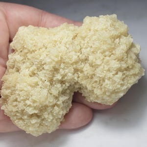 May include: A pale yellow, crystalline mineral specimen with a rough, jagged, and porous texture. The cluster features numerous small, translucent, and opaque crystal formations that create an irregular, organic shape with a dense, granular surface.