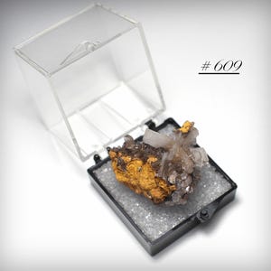 May include: A mineral specimen in a clear acrylic display case. The mineral has a cluster of clear and brown crystals on a golden-brown base. The case is open, revealing the specimen. The text "# 609" is in the upper right corner.
