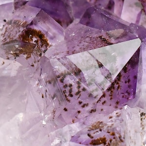 May include: Close-up of a cluster of amethyst crystals. The crystals are a translucent purple color with brown inclusions. The facets of the crystals catch the light, creating a sparkling effect. The overall effect is one of natural beauty and geological wonder.