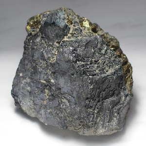May include: A rough, dark gray mineral specimen with a metallic sheen. The surface has a layered texture with patches of golden, crystalline material. The rock is irregularly shaped, showcasing natural geological formations.