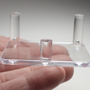 May include: A clear acrylic display stand with three prongs for displaying small objects.