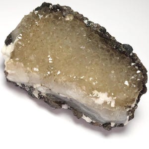 May include: A natural mineral specimen featuring a cluster of small, sparkling crystals in shades of yellow and white. The crystals are encased in a dark, textured matrix, creating a striking contrast. The overall shape is irregular and organic.