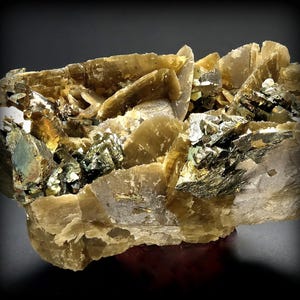 May include: A close-up of a mineral specimen featuring layered, translucent, beige-colored crystals. Interspersed are clusters of metallic, dark green and gold-colored crystals, creating a striking contrast. The overall structure is rough and natural.