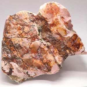 May include: A large, rough-hewn stone with a mix of colors. The stone features shades of pink, brown, and tan, with visible textures and patterns. The overall appearance suggests a natural, unpolished gemstone or mineral specimen.