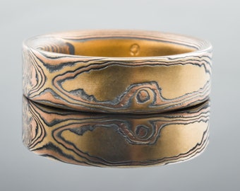 May include: A gold and silver patterned ring with a wide band. The ring has a unique, swirling design.