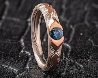 Puede incluir: Un anillo de metal con patrón con una piedra preciosa azul engastada en un engaste de oro rosa.