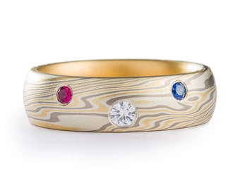 May include: A gold band ring with a patterned surface and three gemstones: a ruby, a sapphire, and a diamond.