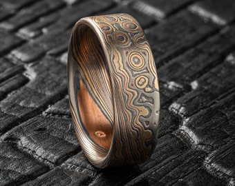 May include: A wide, silver and copper ring with a swirling, patterned design. The ring is made of metal and has a polished finish.