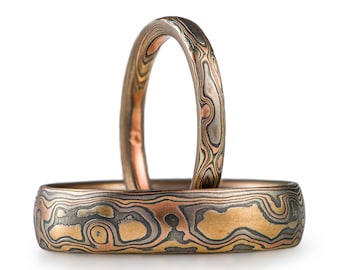 May include: Two matching wedding bands with a unique, swirling pattern of copper, gold, and silver.