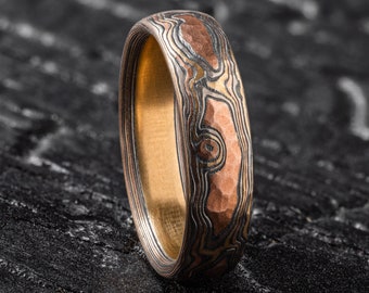 May include: A close-up of a gold and copper patterned ring with a hammered finish. The ring is made of metal and has a unique, organic design.
