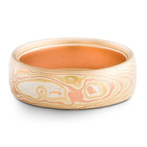 Puede incluir: Un anillo ancho y estampado con un interior de cobre. El anillo tiene un patrón de remolino de blanco, dorado y rosa.