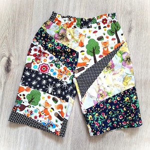 May include: Patchwork shorts with a mix of colourful fabric patterns. The design includes floral, fox, butterfly, and polka dot prints. The shorts have an elasticated waistband and a knee-length cut, suitable for casual wear.