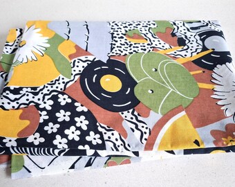 Può includere: Un pezzo di tessuto piegato con una stampa grafica multicolore. Il motivo include margherite bianche, forme gialle, foglie verdi, pois bianchi e neri, linee ondulate e forme astratte nelle tonalità del marrone, nero e azzurro.