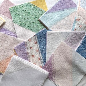 May include: A collection of folded lace handkerchiefs in various colors, including white, black, green, blue, and lavender. The handkerchiefs feature different lace patterns and textures, creating a visually appealing display.