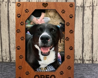 May include: A wooden photo frame featuring a black and white dog named Oreo. The frame is adorned with paw prints and a heart-shaped cutout. The dog is smiling. The name "OREO" is printed at the bottom of the frame in capital letters.