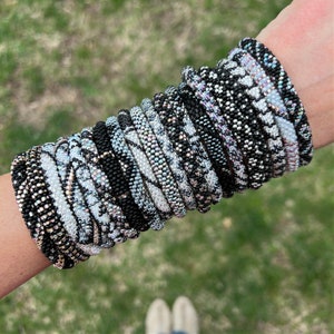 May include: A stack of black and white patterned bracelets with iridescent beads. The bracelets are stacked on a person's wrist.