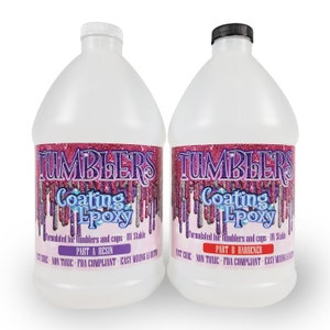May include: Two clear plastic gallon jugs of Tumblers Coating Epoxy. The labels are pink and purple with glitter and the text "Tumblers Coating Epoxy" in a white font. The left jug is labeled "Part A Resin" and the right jug is labeled "Part B Hardener".