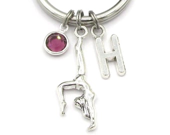 May include: Silver keyring with a gymnast charm, a pink gem charm, and a letter H charm.