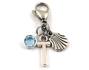 May include: Silver charm featuring a blue crystal, a cross, and a seashell. The charm is attached to a silver lobster clasp.