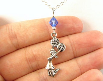 May include: Silver necklace with a charm of a cheerleader holding pom-poms and a blue crystal bead.