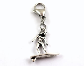 May include: Silver charm featuring a woman surfing on a surfboard. The charm has a lobster clasp for attaching to a bracelet or keychain.